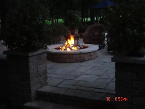 Circular stone fire pit burning on a paved garden terrace at dusk