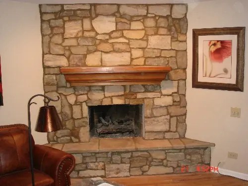 Floor-to-ceiling natural stone fireplace with a timber mantel shelf in a family room