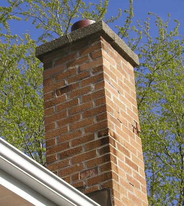 Rebuilt red brick chimney with a cast concrete crown and clay flue tile, seen above a roofline