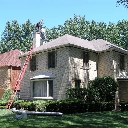 Technician on a roof feeding a stainless steel chimney liner down a chimney